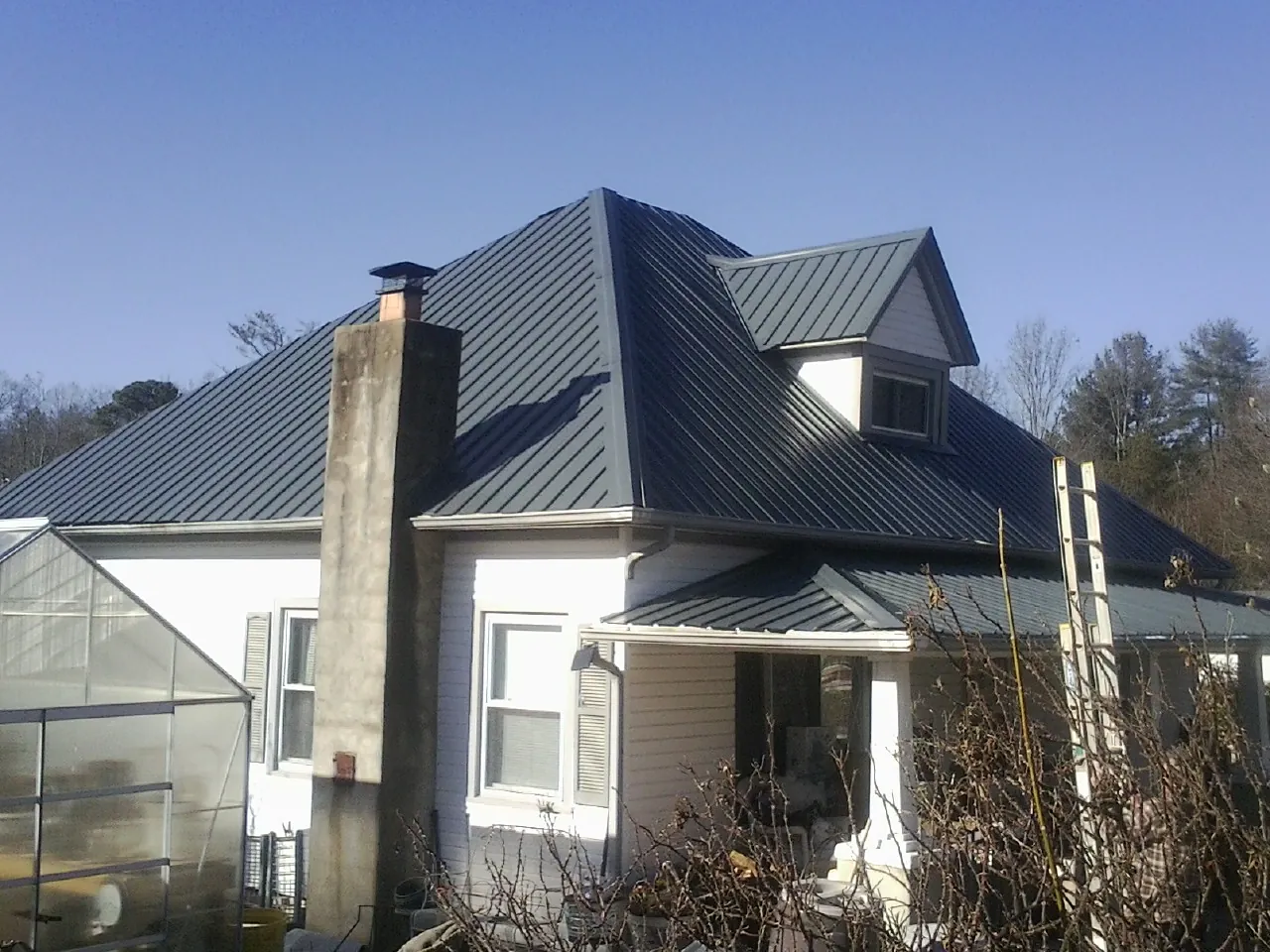 Dark blue standing seam metal roof on a white farmhouse with dormer — Slate & Tile Roof Repair by Roofing Brothers in Waelder