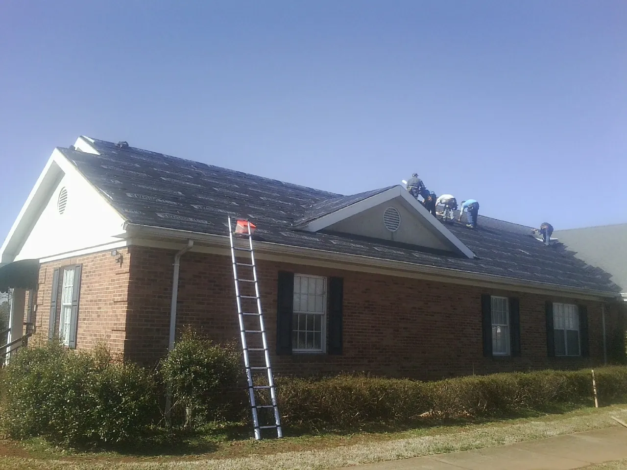 Crew tearing shingles off a brick ranch roof with a ladder set — Emergency Roof Repair work by our crew in Waelder