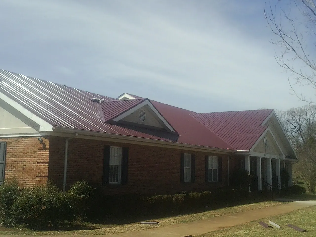 Red metal roof with gabled entries on a long brick building, from a Hail Damage Roof Repair job in Waelder