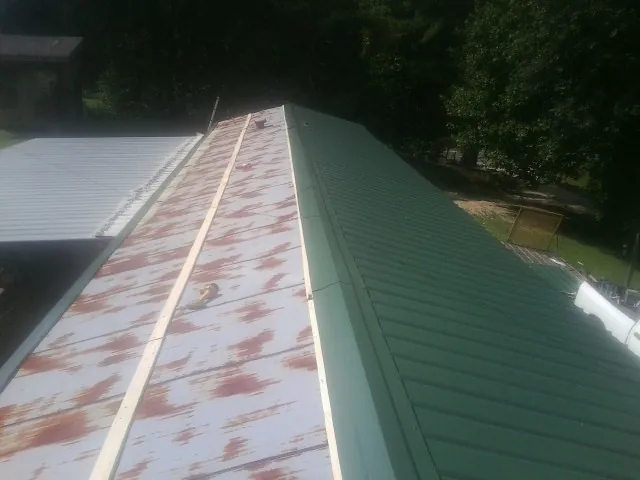 Old rusted panels beside newly installed green metal roofing — Wind Damage Roof Repair by Roofing Brothers in Waelder