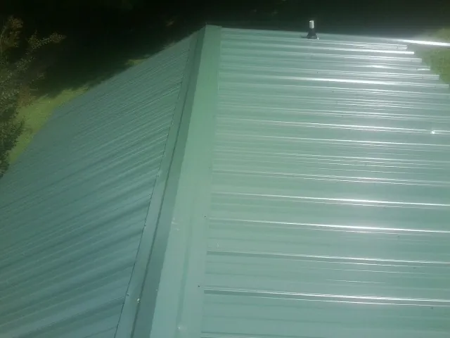 New green metal panels meeting at the ridge of a roof — Flat Roof Repair work by our crew in Waelder