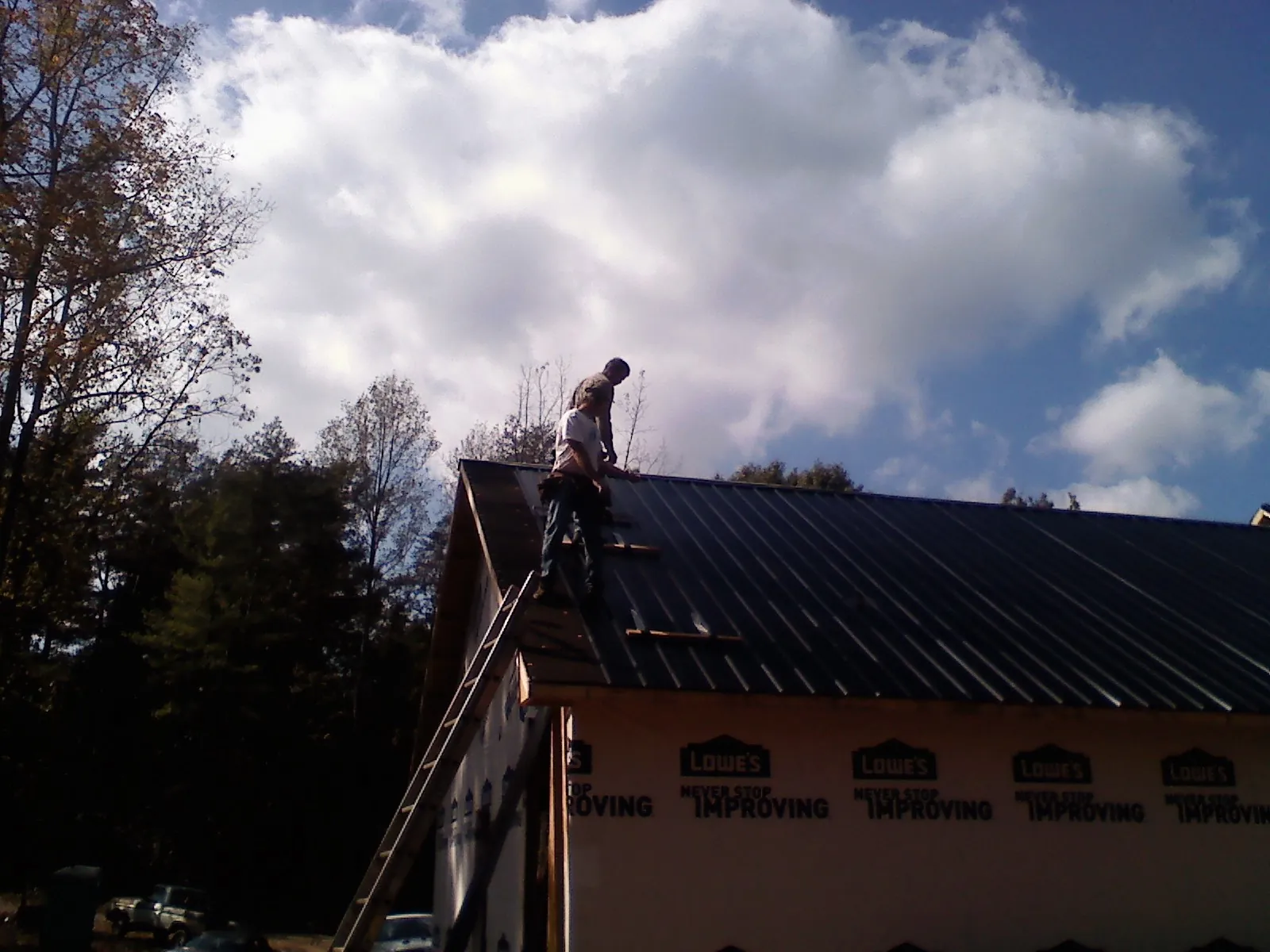 Roofer fastening dark metal panels high against a cloudy sky, from a Roof Inspection job in Waelder