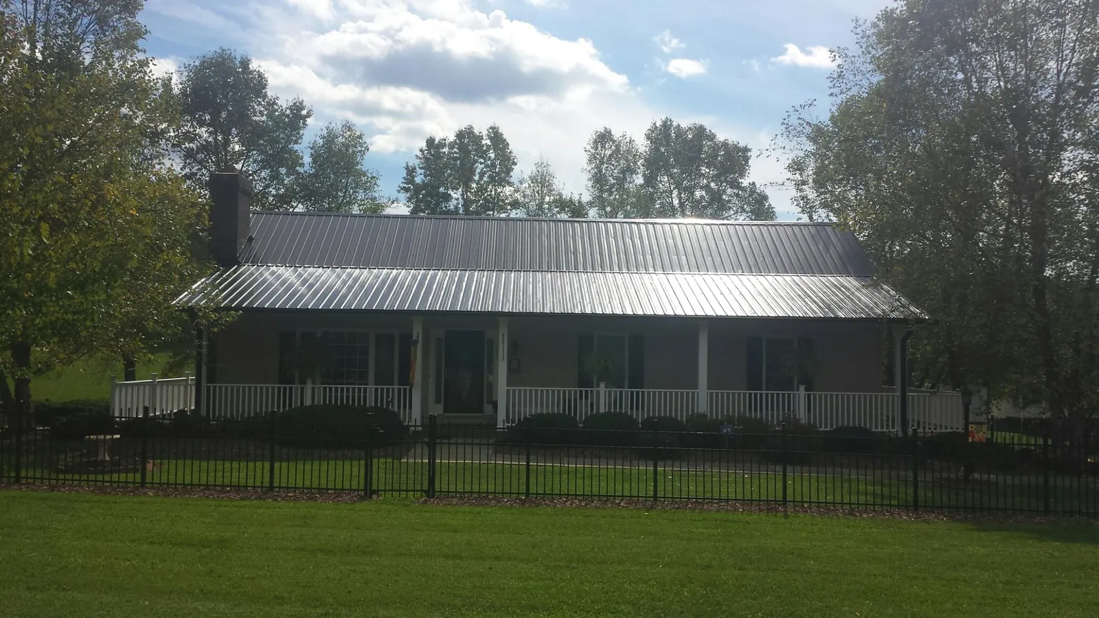 Gray metal roof on a brick ranch with a full width front porch — Gutter Guard Installation work by our crew in Waelder
