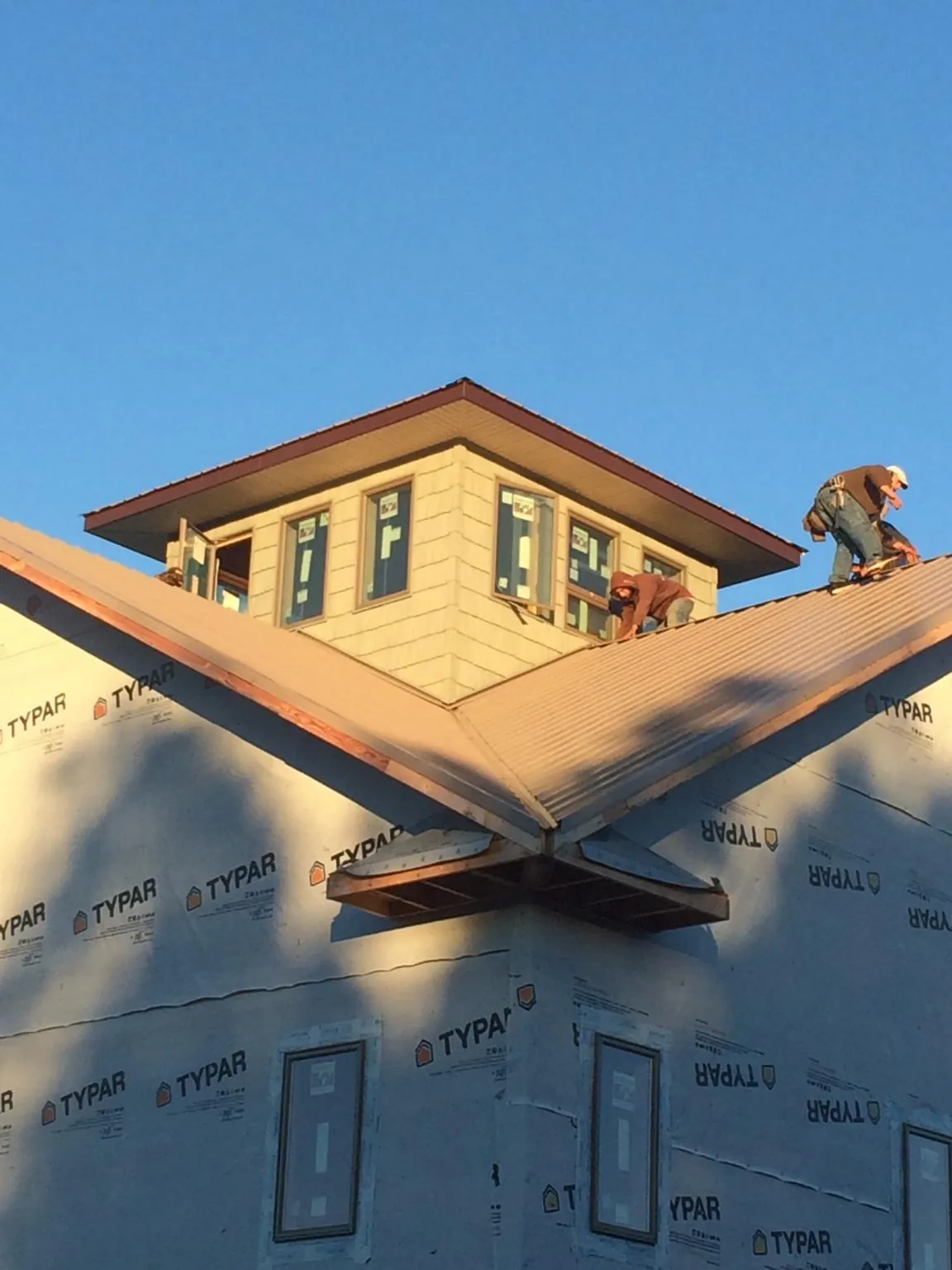 Roofers working around a rooftop cupola on a new metal roof at sunset — Roof Waterproofing in Waelder by Roofing Brothers